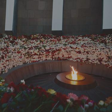 In a circular memorial monument, hundreds of cut roses in all colors form a circle around a lit flame.