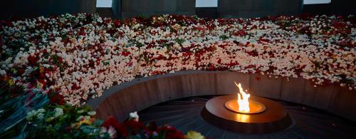 In a circular memorial monument, hundreds of cut roses in all colors form a circle around a lit flame.