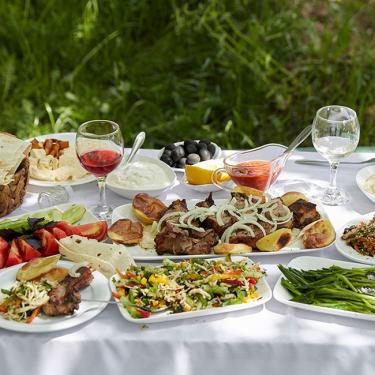 An outdoor table set with various meat and vegetable dishes and drinks.