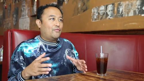 A person sits in a restaurant booth, gesturing with their hands.
