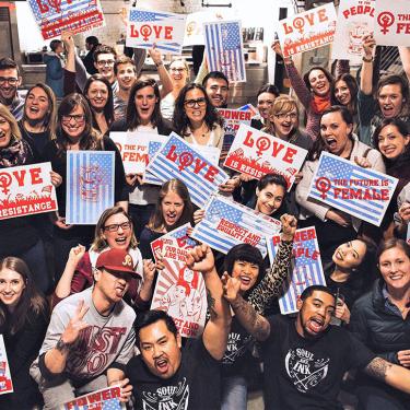 Group of people hold up silkscreened protest signs that read LOVE IS RESISTANCE and THE FUTURE IS FEMALE.