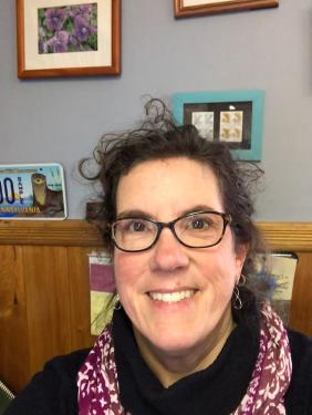 A woman wearing glasses and a purple scarf smiles at the camera. 
