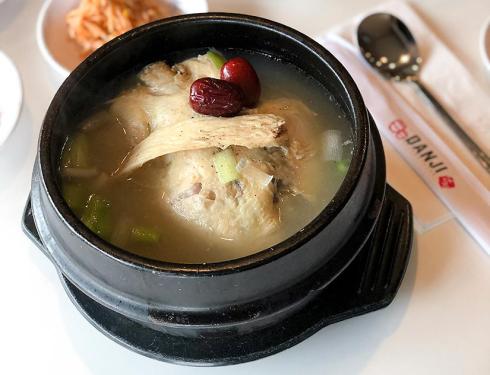 A matte black metal bowl filled with ginseng chicken soup. Diced onion and celery float in the broth and two jujubes garnish the top of the chicken.