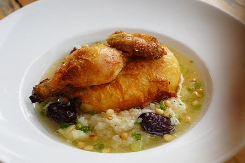 Half a roast chicken sits on a bed of rice in a pool of broth. Two jujubes, pine nuts, and sliced scallions garnish the dish. 