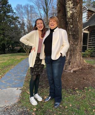A woman in a white sweater and jeans stands to the right of her granddaughter. Both smile at the camera. 