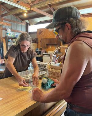 A woman and a man lean over a wooden counter in a shop.