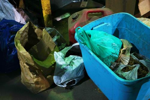 On the right side of the frame is a blue plastic tub filled with plastic shopping bags. There are additional plastic bags full of unknown items on the floor to the left of the tub. 