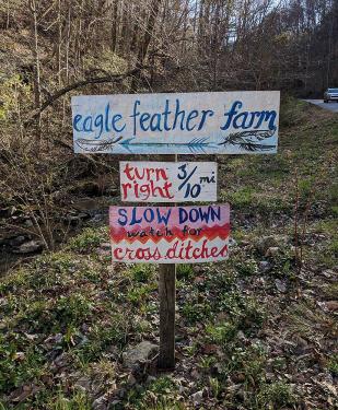 A brightly painted sign reads: Eagle Feather Farm, turn right 3/10 mi, slow down watch for cross ditches. 