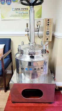 A tall metal machine with a round base and long cylindrical pole rising from the center sits in the corner of a room. 