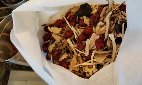 A white cloth bag is filled with a mixture of dried berries and herbs. 