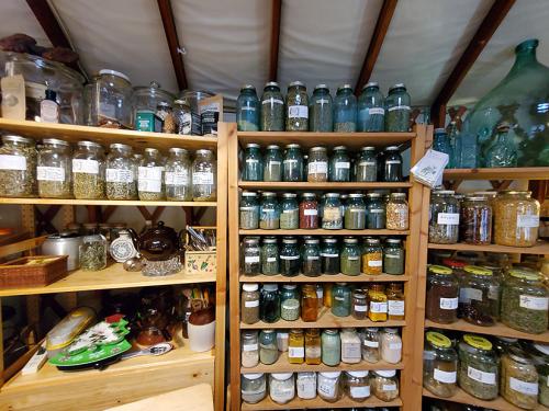 Three wooden shelves hold glass jars of various sizes containing herbal mixes. 