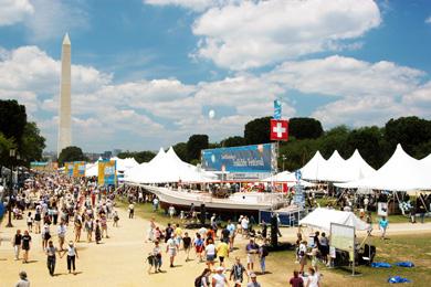 Wide shot of the National Mall, with tents and crowds of people in the foreground and Washington Monument in the background.