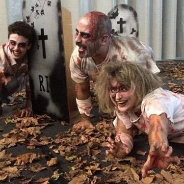 Tres persones fan de zombis esquitxades de sang en un carrer ple de fulles mortes i làpides de cartró.