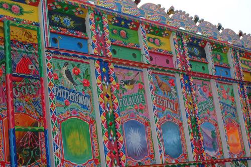 Colorful mural of birds, flowers, geometric shapes, scenes from nature, and the words 2002 SMITHSONIAN FOLKLIFE FESTIVAL SILKROAD PROGRAM.