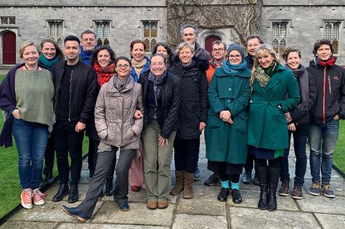 Seventee adults pose outside a stone building, dressed in winter coats.