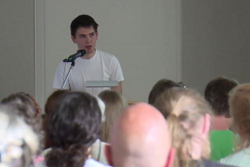 Young man speaks at microphone to an audience.
