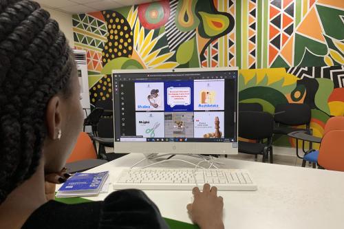 A woman at a computer is looking at images of educational language content with a colorful mural in the background.