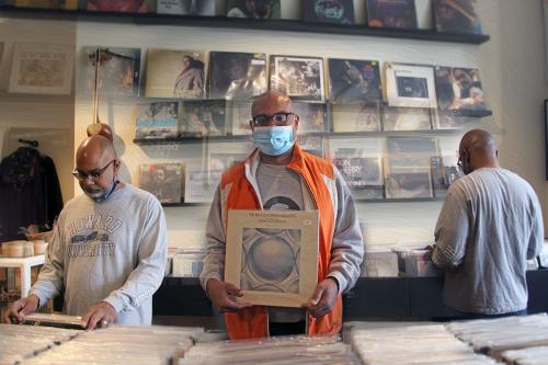 A montage of three photos showing the shelves of a record store and a man, in three separate positions, digging through the stacks. In the center, he holds up an album.