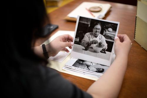 A person, face unseen, holds up archival black-and-white photographs in a library.