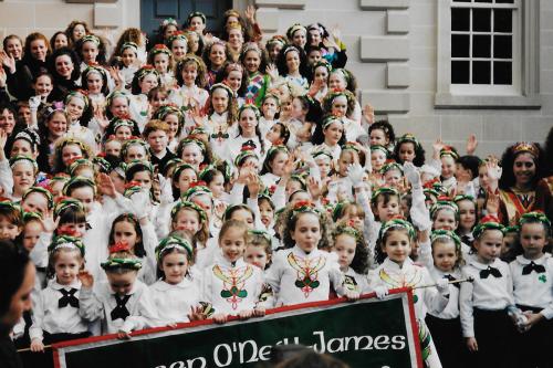 Posed group photo of dozens of young kinds on the steps to a building. they are wearing matching white and green outfits.