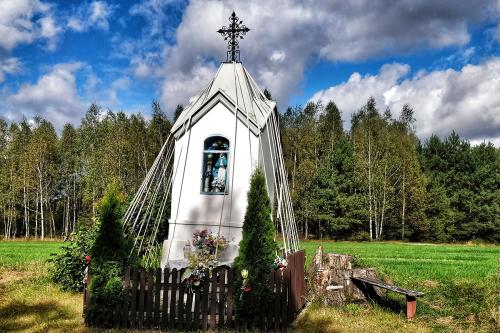 Outdoor shrine, like a miniature church, surrounded by ribbons, picket fence, and shrubs.