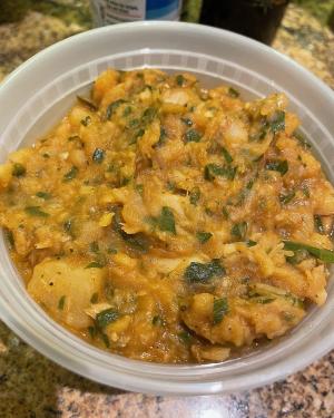 Close-up on a round dish of yellow stew with chunks of white fish and potato and bits of green onion.