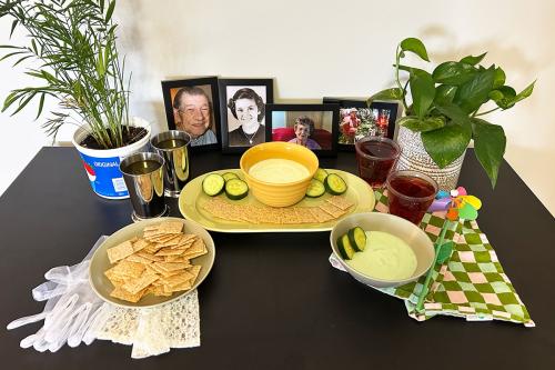 A table set with bowls of pale yellow and pale green dips, crackers, mint juleps, lacey white gloves, a rainbow-colored pinwheel, family photos, and houseplants.