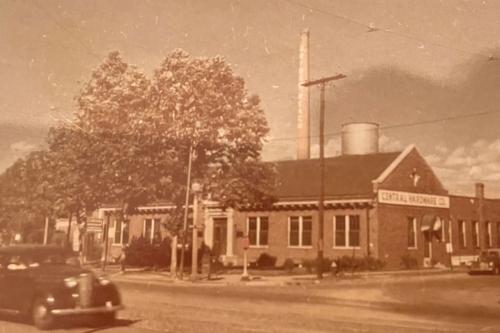 A single-story brick building on a street corner with a sign above the door: Central Hardware. Sepia-toned photo.