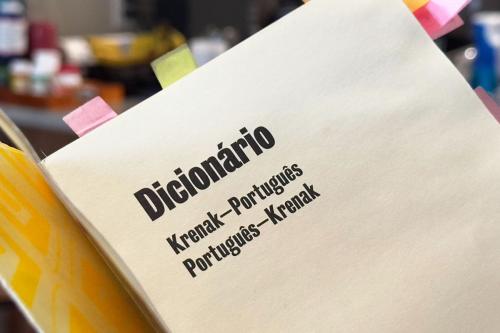 Cover page of a book with text: Dicionário. Krenak-Português, Português-Krenak. Interior pages are marked with pink and yellow sticky notes.