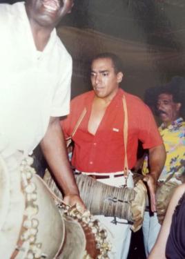 Three men stand or process, each playing a conical two-headed drum hung around his neck. Old color photograph.