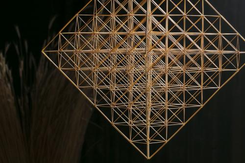 Mobile made of straw in the shape of a cube, made up of octahedrons, with a faint bouquet of straw against a black background.