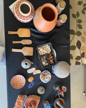 Overhead view of ceramic pots, containers of clay materials, and wooden spatula-shaped tools set on a table.