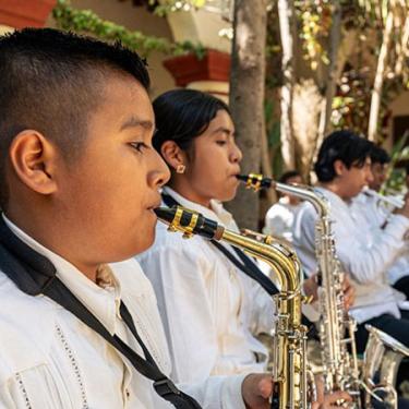 Close-up on student musicians playing saxophones in white shirts and black pants. 