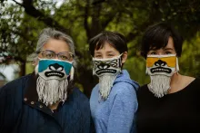 Three people, three generations of a family, pose outdoors wearing decorative beaded face masks.