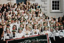 Posed group photo of dozens of young kinds on the steps to a building. they are wearing matching white and green outfits.