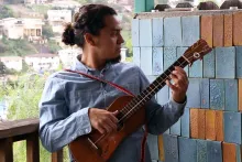A man holds up and plucks a jarana (small stringed instrument).