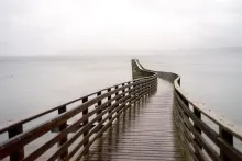 A long wooden dock stretches across a gray sea to the horizon.