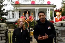 Two young people stand in front of a white house adorned with decorations.