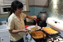 A woman holds up a piece of chicken pie, with the remainder next to her on the stove.
