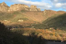Sunlit mountain, with roofs of homes and a bell tower peaking through the trees.