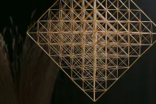 Mobile made of straw in the shape of a cube, made up of octahedrons, with a faint bouquet of straw against a black background.