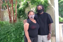 A Black couple stands outside an office building, arm in arm, face masks on.